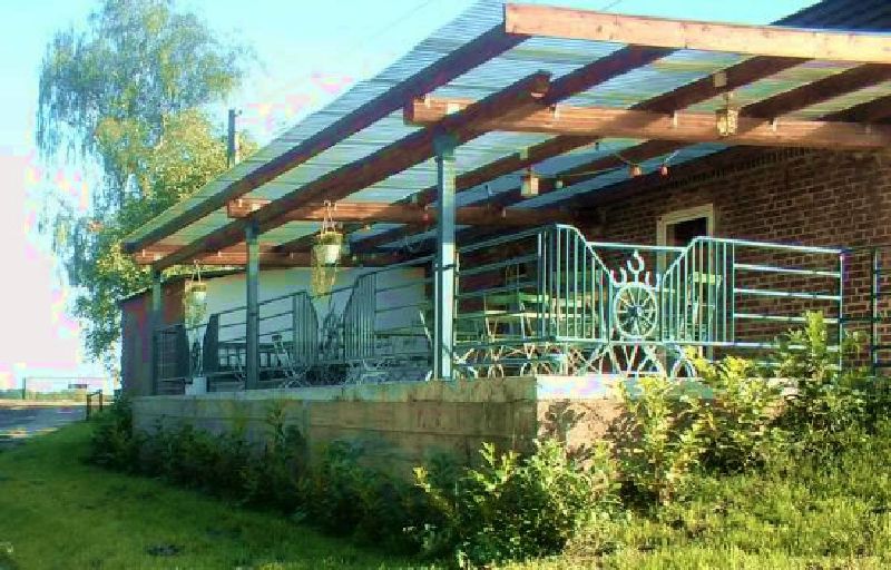 Außenansicht des Partystalls: überdachte Terrasse mit Holzbalken, schmiedeeisernem Geländer mit Wagenrad-Motiv und Backsteinfassade.
