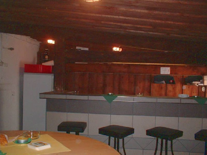 Theke aus dunklem Holz mit gepolsterten Barhockern, daneben ein Kühlschrank.